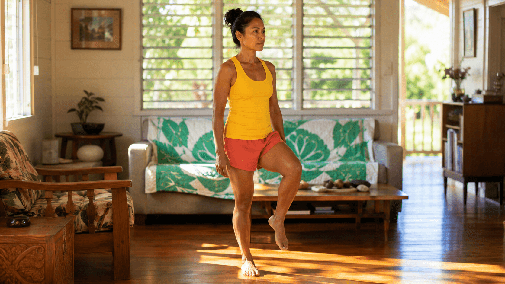 Woman in a yellow tank top standing on one leg in a Hawaiian living room with jalousie windows, mid-stance balance test